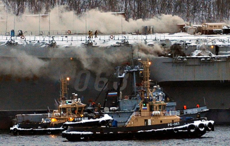 Several small boats tend to the stricken aircraft carrier, tied up at a shipyard in Murmansk, Russia