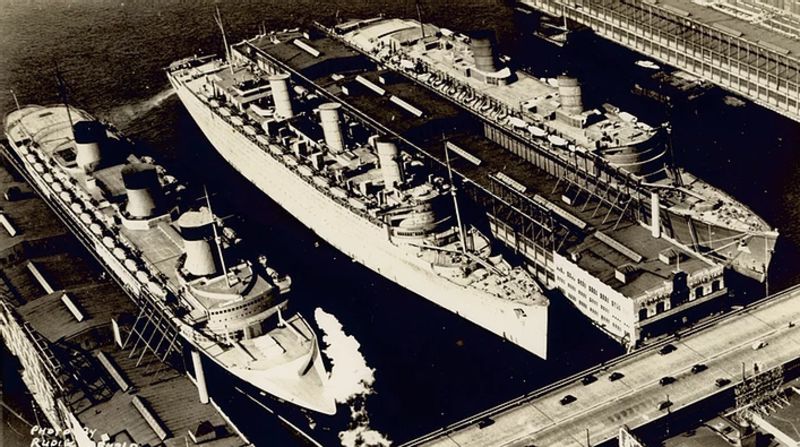 The world’s three largest ships moored together for 2 weeks in March, 1940. The 83,000 ton Normandie was still laid up under a caretaker crew, the 81,000 ton Queen Mary in the middle had recently finished conversion to a troop transport and was preparing to set sail, while the newly finished 83,000 ton Queen Elizabeth at the far right had just made a covert dash across the Atlantic from Scotland under the cover story of sea trials, and would stay for a few months before setting sail for Singapore to complete conversion to a troop ship. 