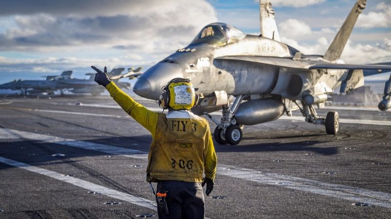 A sailor directs the pilot of an F/A-18C Hornet from the “Blue Blasters” of Strike Fighter Squadron (VFA) 34 on the flight deck of the carrier Carl Vinson. The Legacy Hornet completed its sundown cruise when the Vinson returned to San Diego. (MC2 Sean M. Castellano/US Navy)