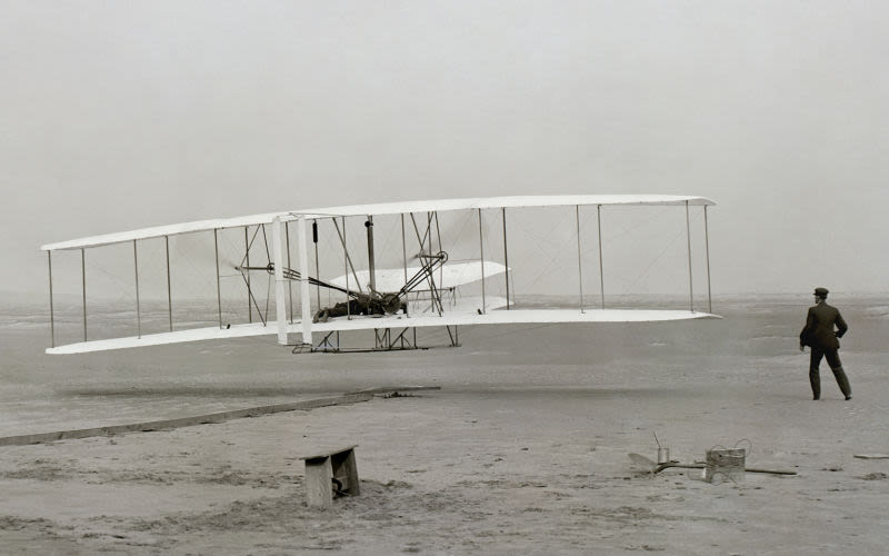With Orville Wright lying prone at the controls, and his brother Wilbur running alongside, the Wright Flyer makes its first controlled flight from the dunes of Kitty Hawk, North Carolina. (US Library of Congress)