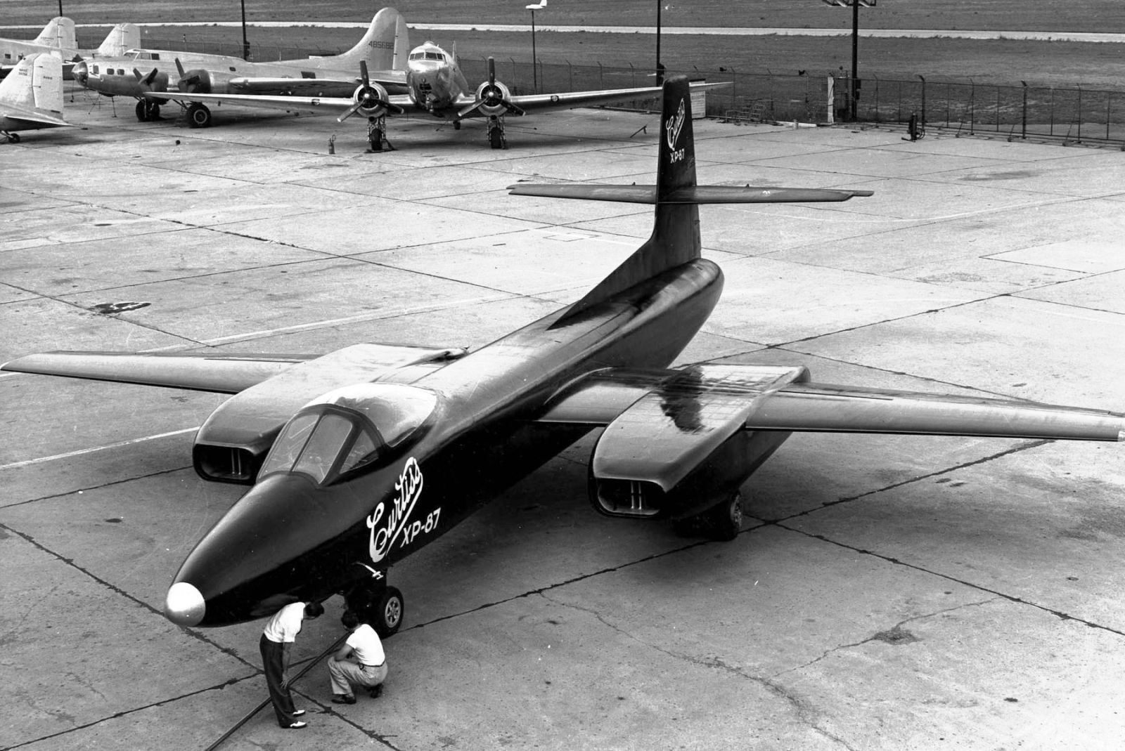 The XP-87 (later XF-87), likely photographed at the Curtiss factory in St. Louis. The size of Blackhawk is evident when compared to the two men examining the front wheel. A B-17 and DC-3 are visible in the background. (US Air Force)